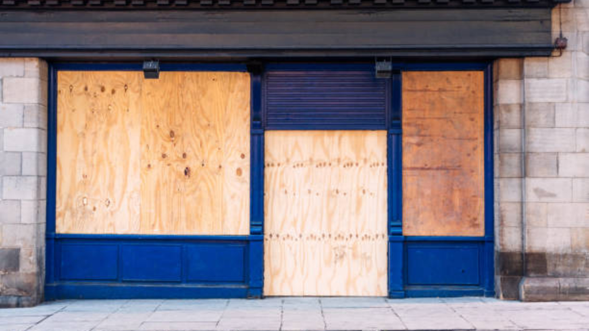 A traditional British shopfront, closed and boarded up with wooden boards.